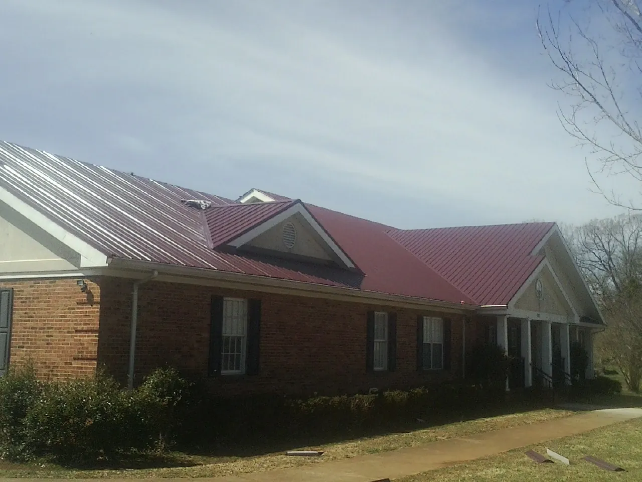Red metal roof with gabled entries on a long brick building, from a Hail Damage Roof Repair job in Elgin
